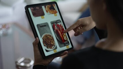 Person scrolling through food menu at online app delivery order. Over the shoulder of a young woman ordering meal