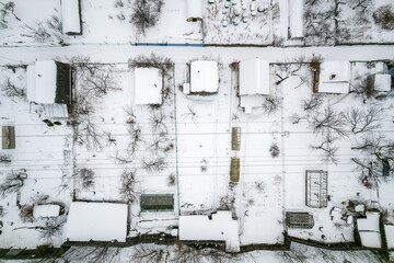 Aerial view of coniferous winter forest and a small houses.. Flying above frozen trees and snow covered ground of dense forest and a small houses for glamping.