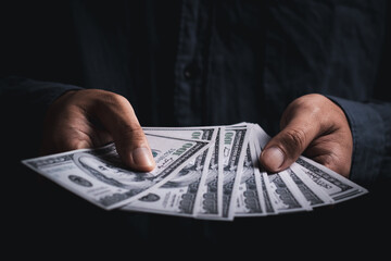 Businessman hand holding money. Saving money, income, earning and investment concept. Dark tone....