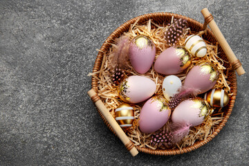 Golden and pink colored eggs and  feathers in wicker plate
