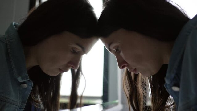 Troubled young woman looking at bathroom mirror suffering mental distress. Worried person feeling anxiety