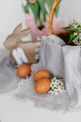 Easter spring background with wooden bunny, wicker basket with flowers, pink tulips and brown dyed eggs on gray napkin. Mock up. Space for text