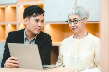 Fototapeta premium Young Asian business man in formal clothing showing something on digital tablet to senior female boss and manager wearing eyeglasses while in a meeting and training on technology