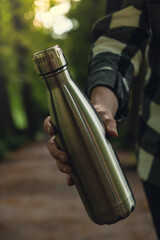Close-up of Unrecognizable female hand holding Water bottle. Reusable steel thermo water bottle in...