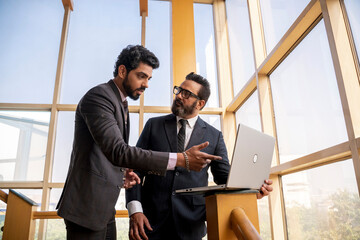 Indian businessman using laptop showing project detail and discussing with his partner or manager.