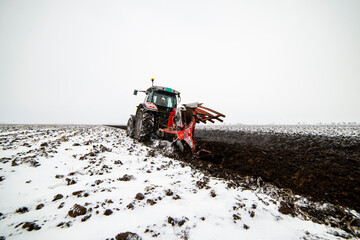 The tractor is working in the field, preparing the soil in winter for spring sowing
