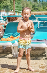 Preschooler with wet hair cowers from wind after swimming in pool. Boy stands shivering from cold...
