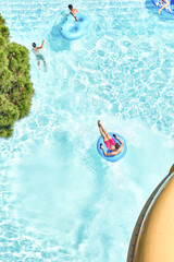 People relax on inflatable rubber rings in swimming pool with clear blue water. Fun activities in...