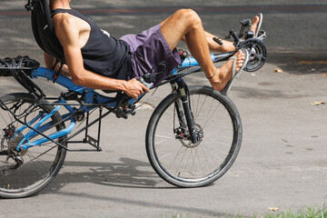 Fototapeta na wymiar Boy in Shorts and Flip-Flops riding a Particular bicycle in a Lying down Position and with the Handlebars along the Sides