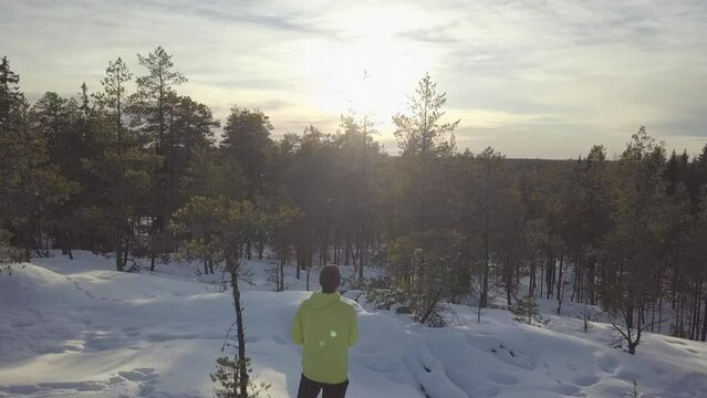 Winter hiking man on mountain top in Ice cold Arctic forest watching sunset view