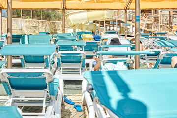 Fototapeta na wymiar Blue sun loungers put in rows under transparent canopy. Sun-protection cover above deck chairs near swimming pool in touristic water park