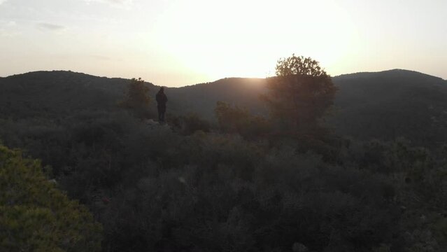 Drone reveals silhouette of man hill scape during sunset, valley and bright sky contrast