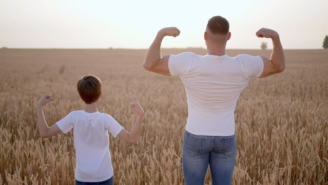 Father and son showing muscles biceps. Father man son boy child teenager having fun sunset sun summer field, Concept childhood friendship care healthy lifestyle sports activity happy family together.