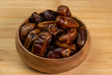 Dates fruits in wooden bowl on wooden background close up. Eating dried fruits. Vegan, vegetarian food