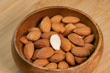 Almond nuts in wooden bowl on wooden background close up. Product rich in minerals and vitamins. Almond kernels. Healthy skin and hair and natural healing oil treatment