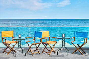 Small glass tables and colorful chairs on sea embankment on summer day. Fancy open air restaurant for tourist at summer tropical resort