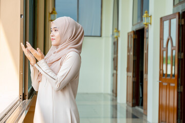 The image of an Asian Muslim woman in the Islamic religion in hijab in cream color. She was praying in a beautiful mosque out of respect for God.