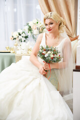 Bride with a bouquet in her hands in a long elegant dress in a festive interior.