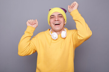 Image of festive happy cheerful man wearing beanie hat and yellow casual hoodie standing isolated...
