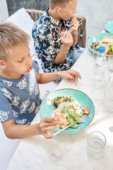 Hungry boys eat delicious dinner sitting at table in restaurant closeup. Preteen children enjoy fresh healthy food in cozy cafeteria