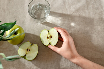 Hand holding half of green apple. Fresh fruits and glass of water on table, healthy nutrition...