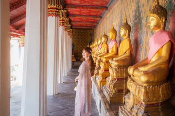 Young woman wearing Thai dress with accessories carrying a bag at Wat Arun Ratchawararam where many Buddha statues are row It is a popular destination for tourists around the world. Bangkok, Thailand