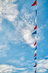 Garland of colorful triangle flags hangs under blue sky with light clouds bottom view. Holiday decoration for festive party on nice sunny day