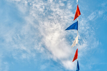 Garland of colorful triangle flags hangs under blue sky with light clouds bottom view. Holiday decoration for festive party on nice sunny day