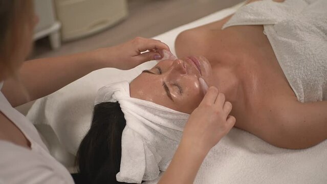 a woman master makes a facial skin massage with special stones to a woman in a white towel. real time video. High quality Full HD video recording