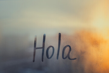 lettering Hola in Spanish language is Hello in english on foggy glass on sunset window © ksenija1803z