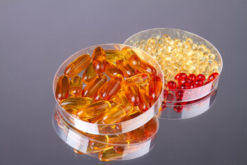 Close up two petri dishes with vitamin pills. Reflective gray background.