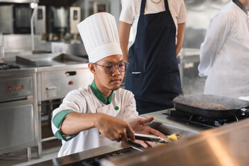 Portrait Asia young man in chef uniform cooking steak fire with student woman assistance chef at...
