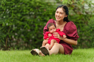 Naklejka na ściany i meble mother holding with newborn baby while sitting in the grass field