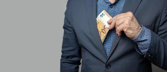 Well dressed man puts a bunch of money in his jacket pocket, euro banknotes, the paper currency of...