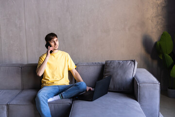 Young man using laptop while talking on phone on the couch