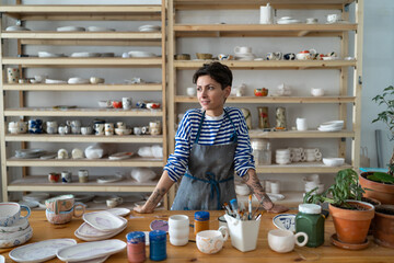 Ceramic business. Self-employed successful female pottery artist working as freelancer in workshop, create unique ceramic items in studio, smiling woman potter at workplace, make handmade kitchenware - obrazy, fototapety, plakaty
