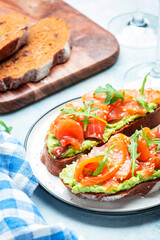 Avocado and salmon sandwich on rye bread with guacamole sauce, arugula and sesame seeds on plate, blue table background, top view