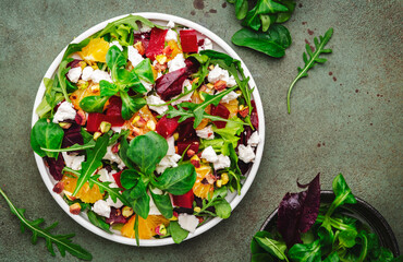 Beet, soft cheese and orange healthy salad with arugula, lamb lettuce, mini chard and pistachios, rusty green kitchen table.. Fresh useful dish for healthy eating
