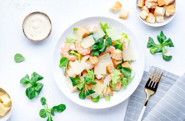 Caesar salad with shrimp, iceberg and lamb lettuce, croutons, parmesan cheese with caesar dressing. White table background, top view