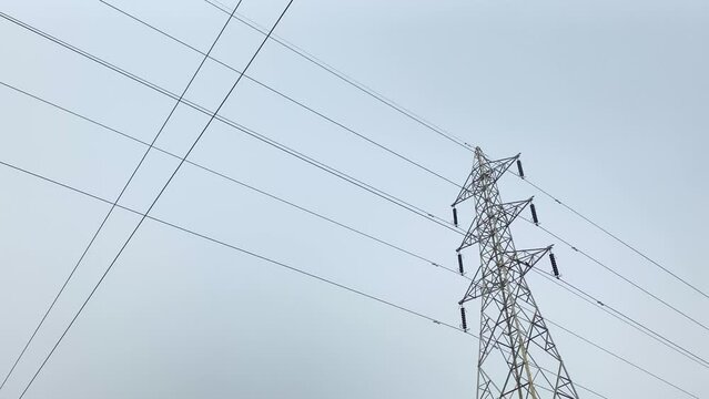 A low-angle shot of a high voltage electricity pylon against a blue sky, depicting the power and infrastructure of modern society.