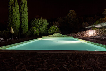 Illuminated swimming pool on the Montemassi hillside surrounded by cypresses and oleanders n the province of Grosseto. Italy
