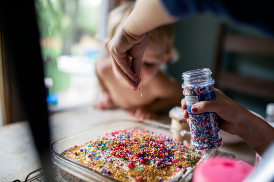 Girl decorating freshly baked cake with plenty of sprinkles