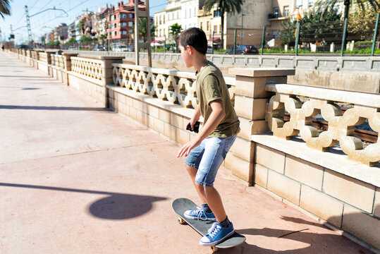 Rear view of young skater boy riding on promenade in a sunny day
