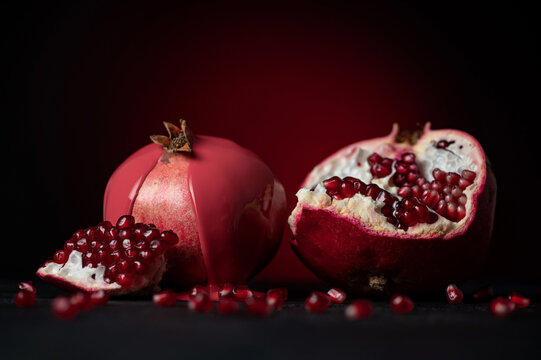 Ripe juicy pomegranate. Pomegranate grains on black surface. Broken pomegranate. Fruit is watered with red paint. Bright fruits. Proper nutrition. Maroon background. Still life. Side view. Copy space.