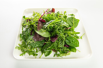salad mix of fresh herbs, arugula, chard, spinach in a plate on a white plate, top-side view