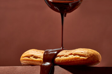 Chocolate eclair is poured with glaze on a brown background.