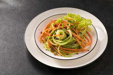 fresh vegetable salad of carrots with cucumber on a white dish and a gray background, serving, close-up