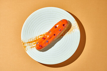 Orange eclair in a plate on an orange background