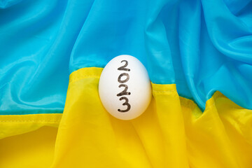 One chicken white egg with the text 2023 lies on the flags of Ukraine, a holiday and culture