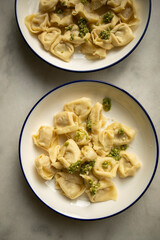 two plates with ready-made hot ravioli with pesto sauce and grated cheese close-up. dumplings ready to eat top view. ravioli in a white plate on a white marble table
